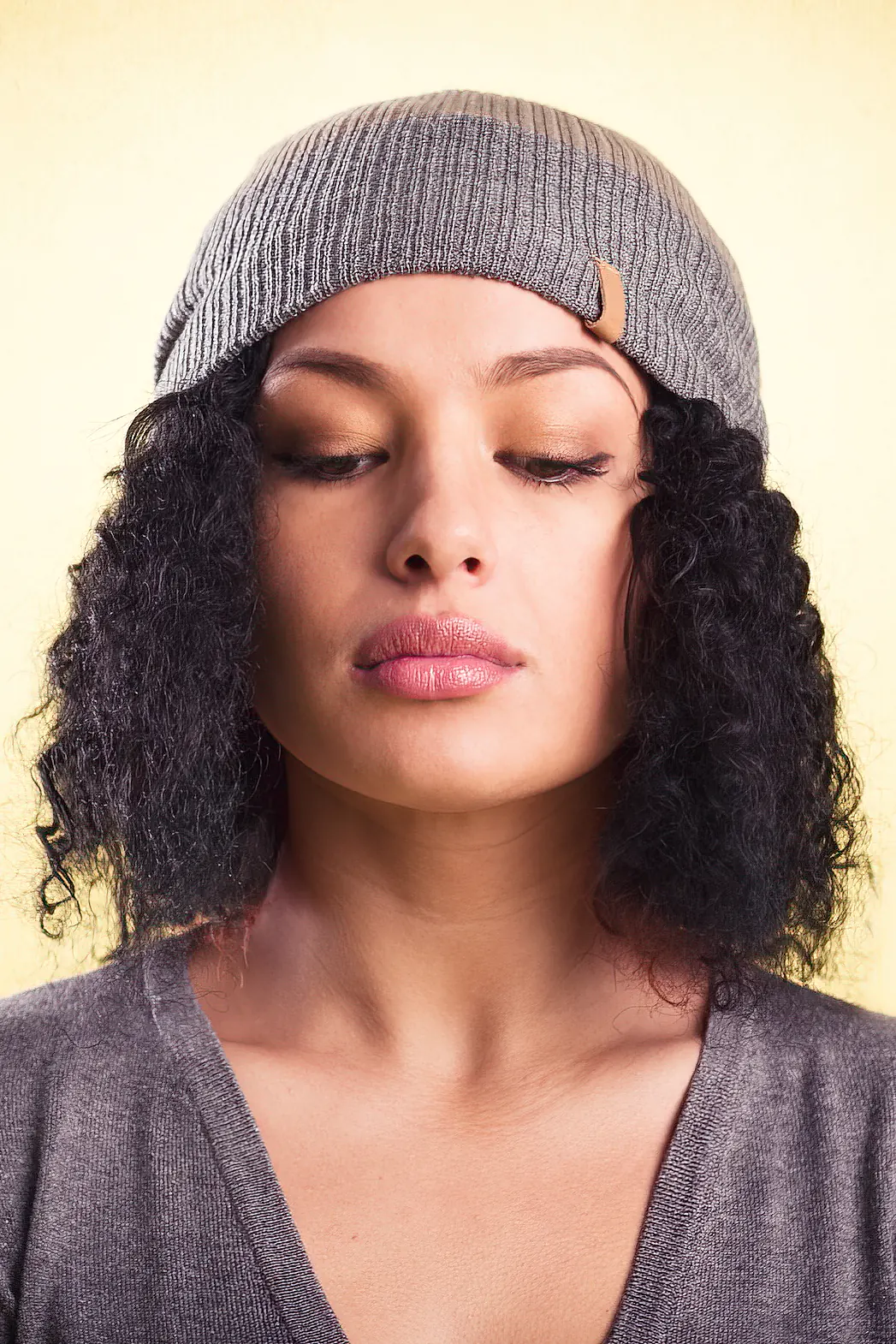 Hip girl with half closed eyes wearing a gray beanie isolated on yellow background