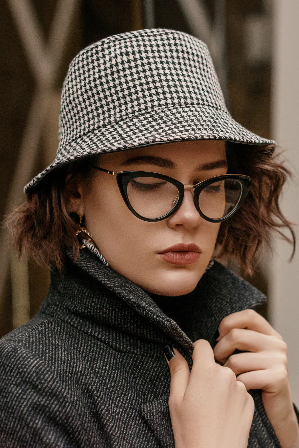 Outdoor close up fashion portrait of young elegant woman wearing trendy checkered bucket hat, stylish cat eye glasses, coat