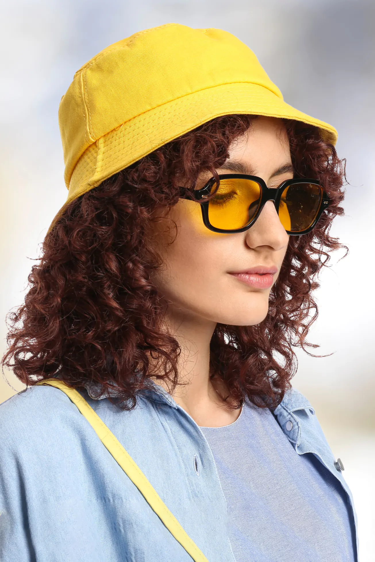 Young woman with curly hair in stylish sunglasses wearing yellow bucket hat on white background